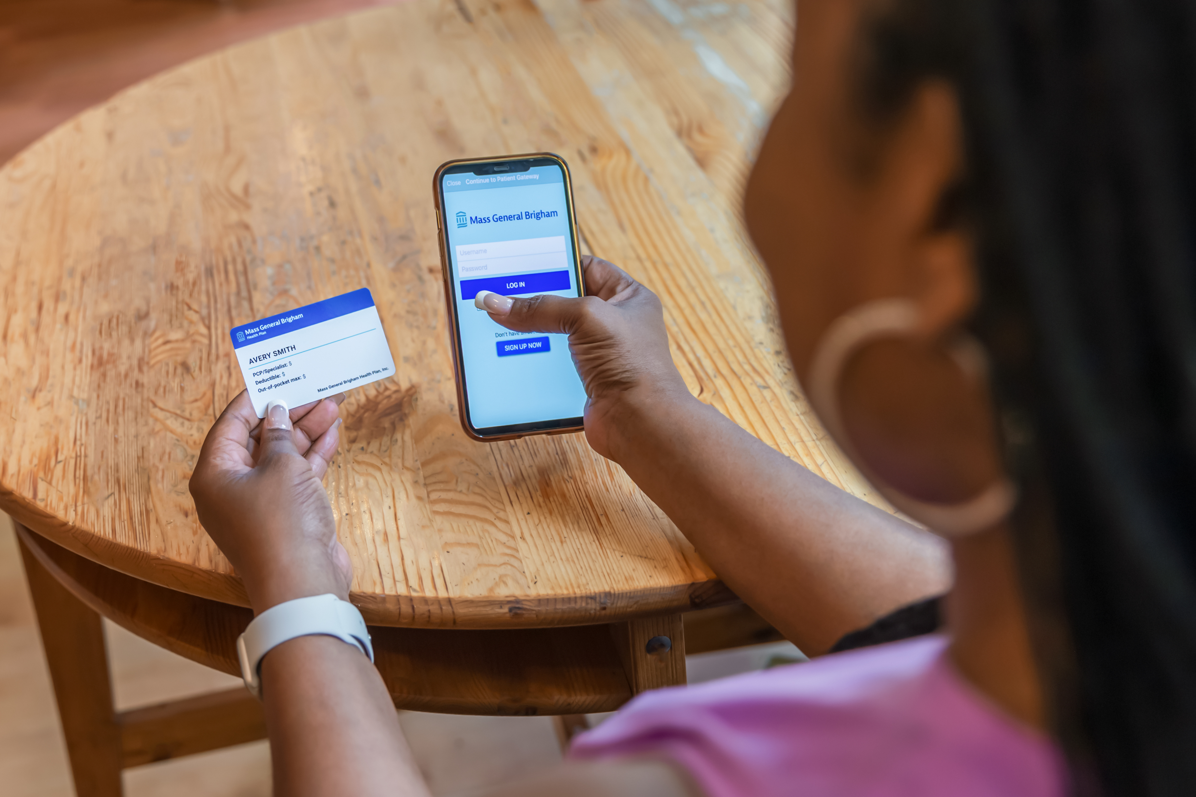 A woman looking at the Health Plan Member app on her phone next to her Mass General Brigham Health Plan member ID card