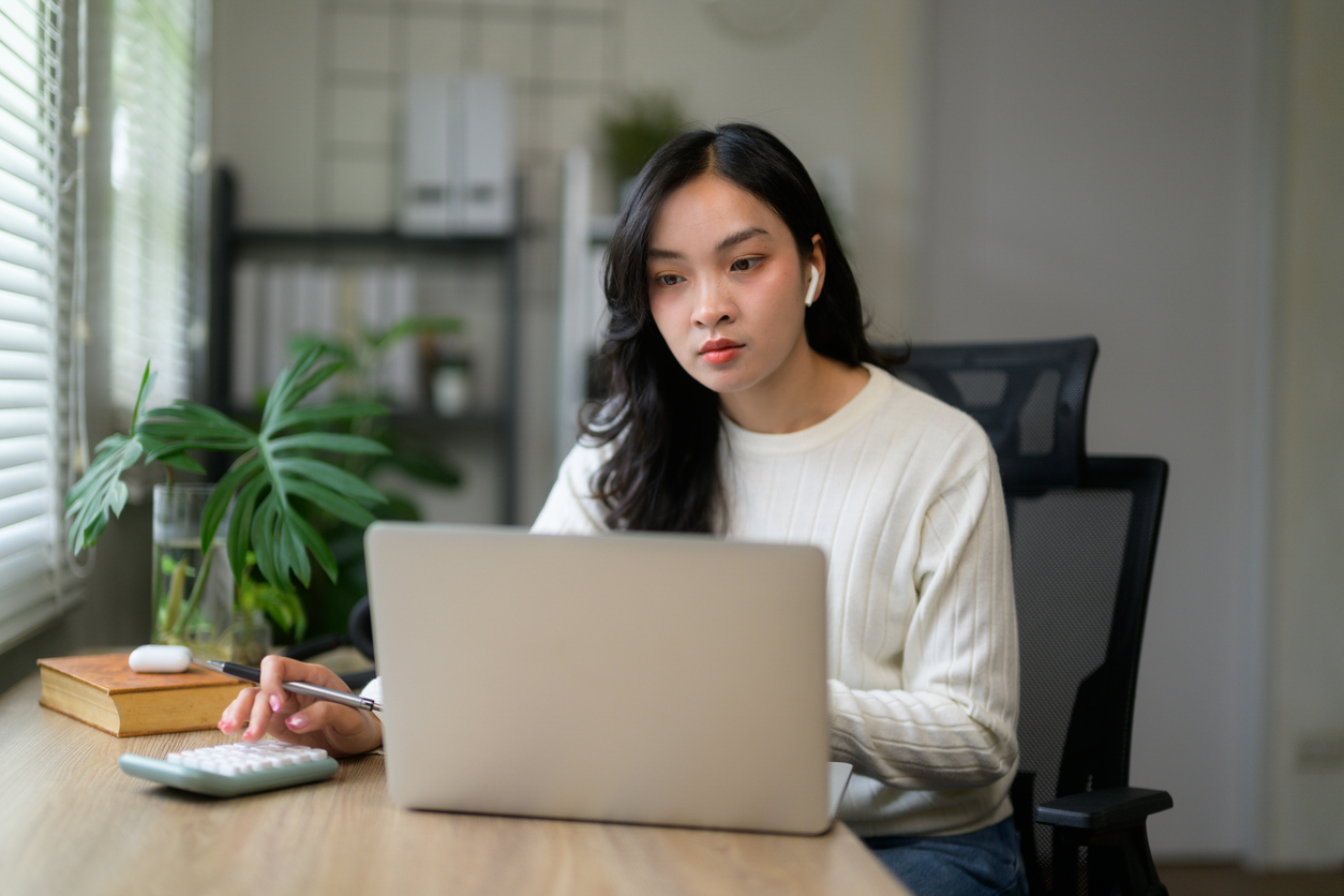 Woman sitting at desk in front of laptop using a calculator