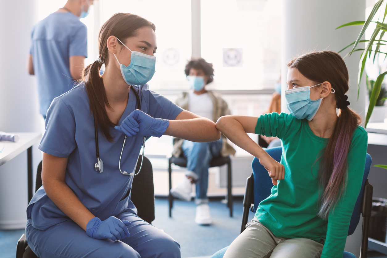 Elbow Bump Greeting. Teen Girl In Medical Mask Bumping Elbows Meeting Nurse Doctor In Hospital Indoor. Social Distancing And Keeping Safe Distance For Covid-19 Protection Concept