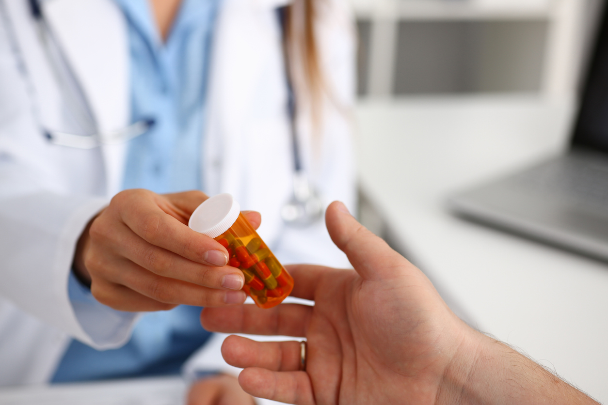 Female medicine doctor write prescription at worktable while patient hand hold jar of pills. Panacea and life save, prescribing treatment, legal drug store concept. Empty form ready to be used
